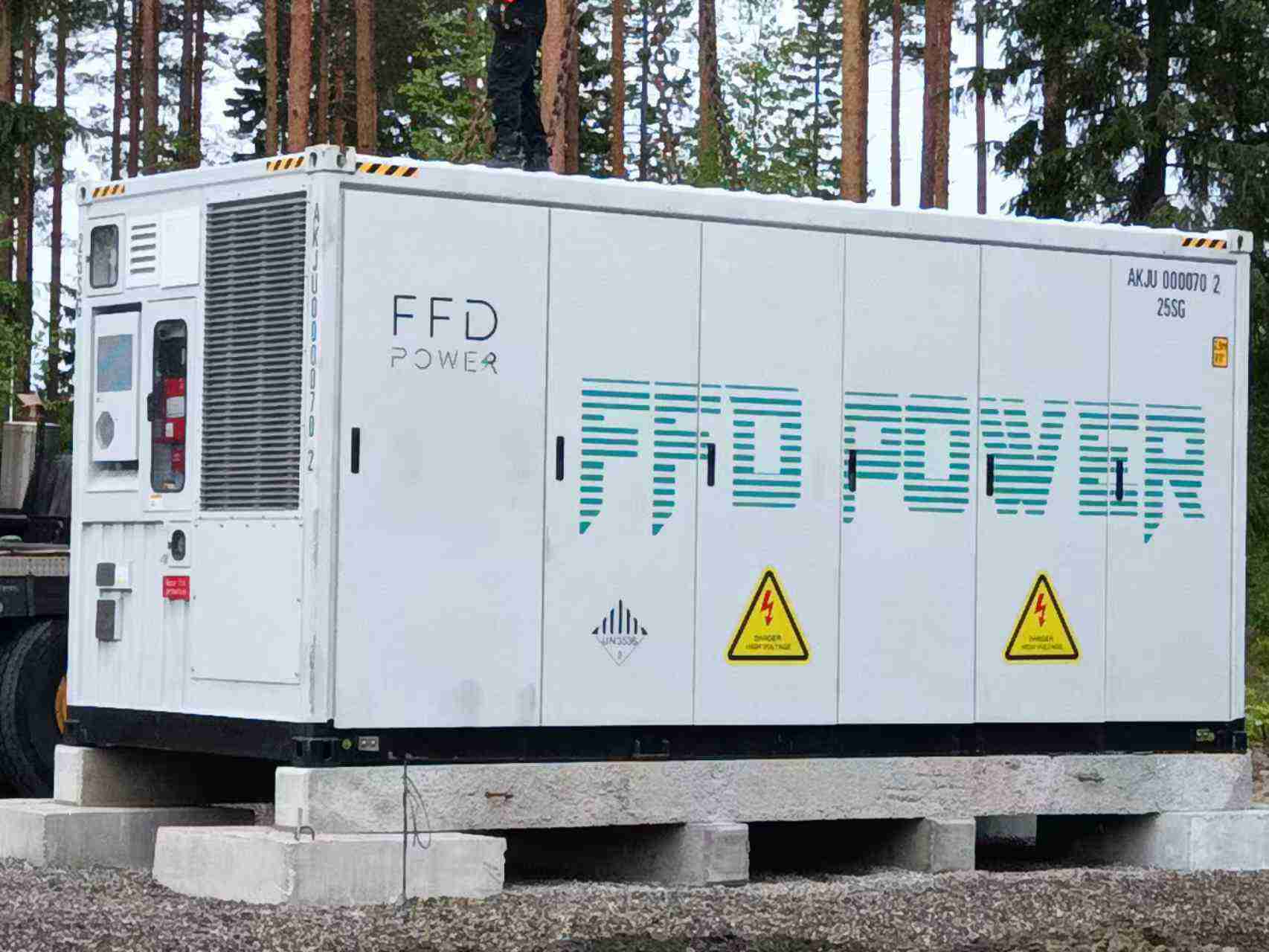 “Side view of the FFD POWER energy storage container mounted on concrete blocks, showing access panels and high-voltage warning labels.”