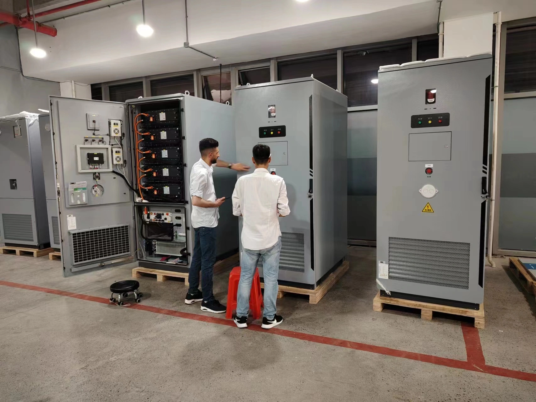 Palestinian delegation visiting FFD POWER, reviewing microgrid power cabinets and control equipment in the workshop.